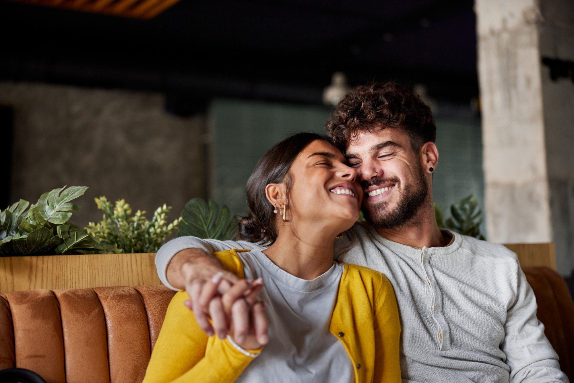 A couple laughing together on a café sofa, cheek to cheek